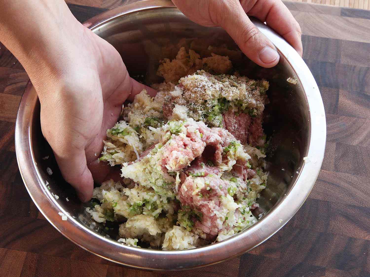 Meat and cabbage being mixed by hand in a bowl.