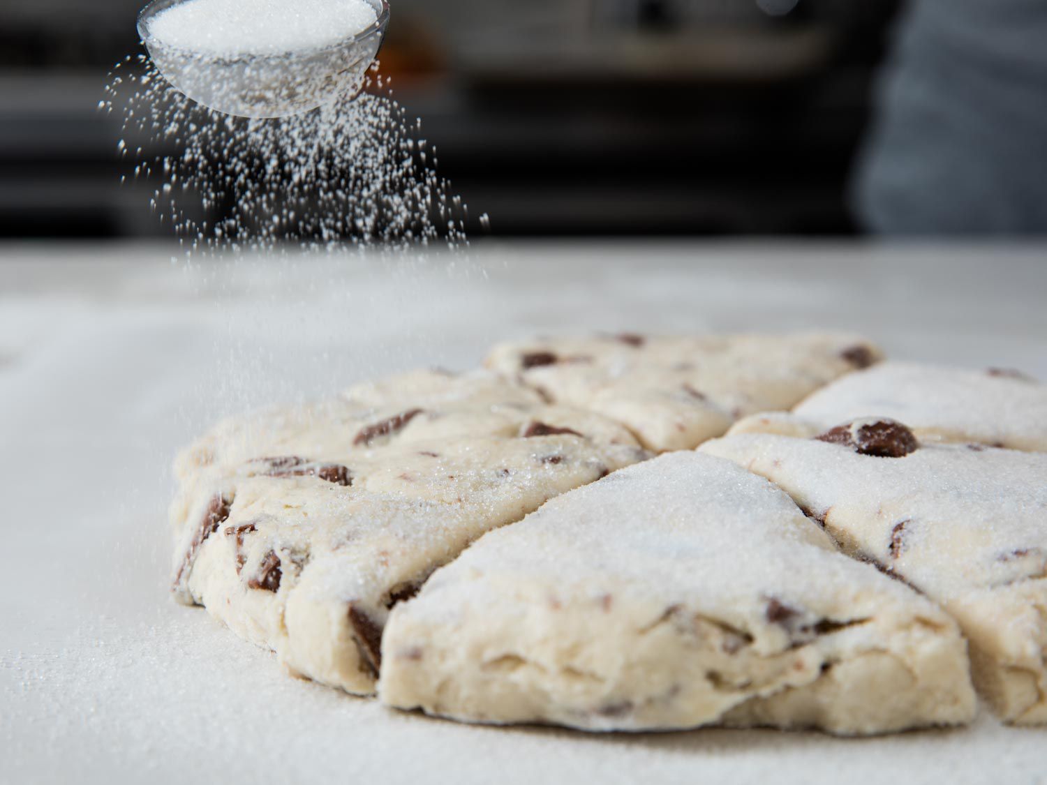 Sprinkling sugar over wedges of chocolate chip scone dough.