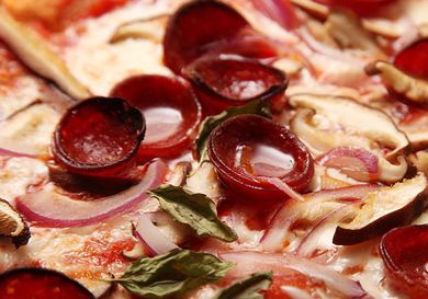 Cooked, curled pepperoni with tiny pools of fat on the surface of a pizza. 