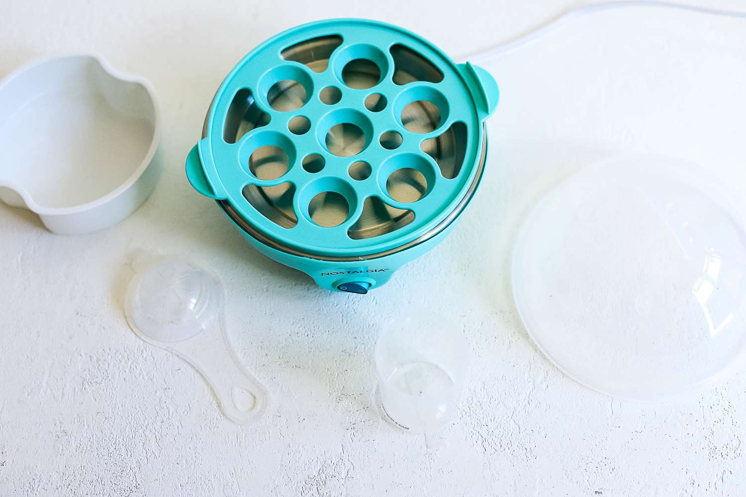 All of the parts of an egg cookers sitting on a white surface