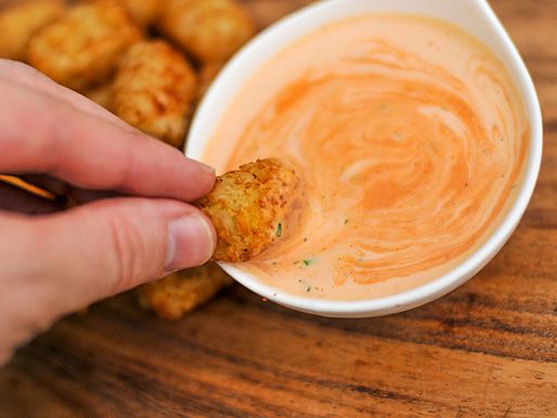 Tots are dipped in a small bowl of franch dressing.