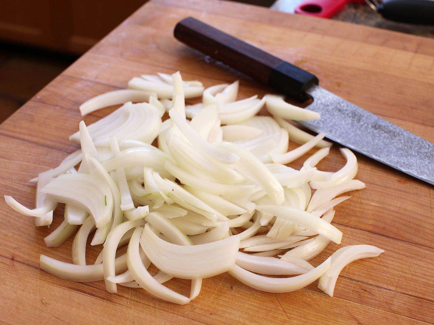 Sliced onion and a knife resting on a cutting board. 