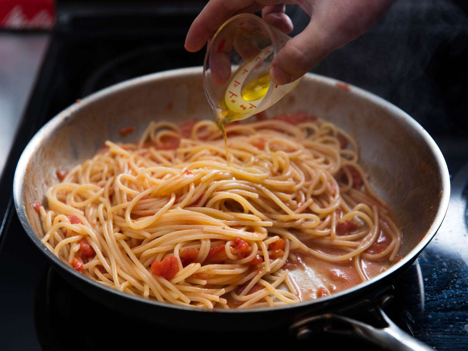 Olive oil being poured over the pasta and pasta sauce.