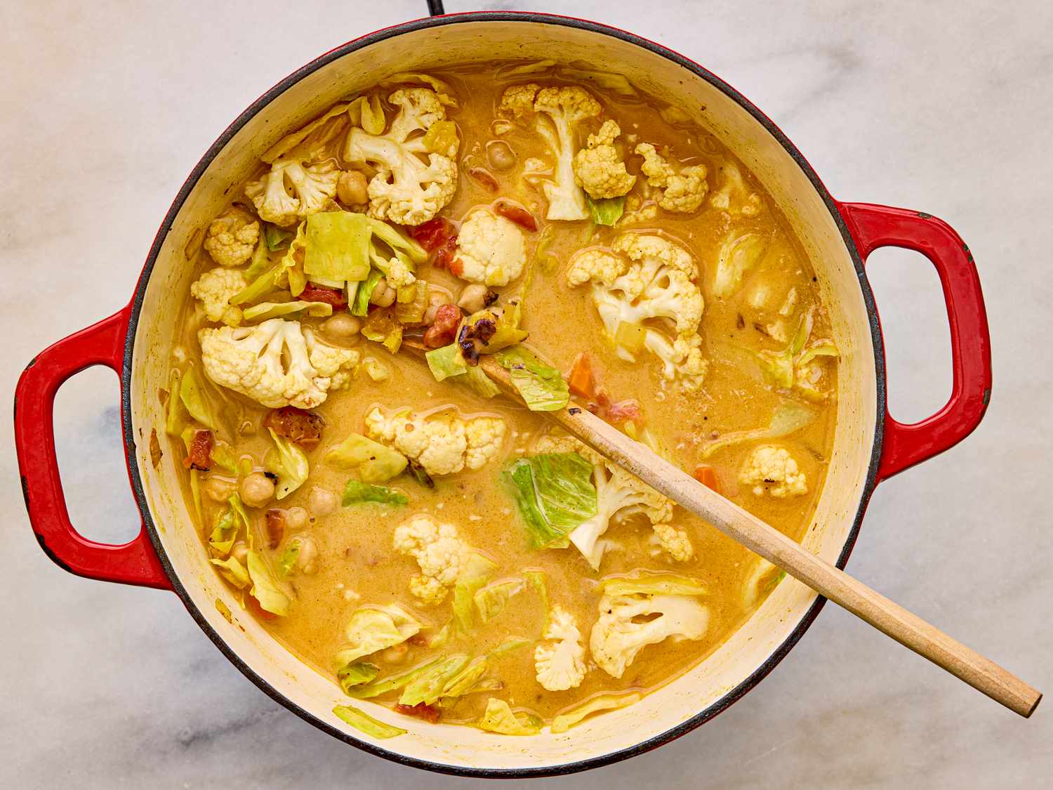 A pot of cabbage soup with cauliflower in a red pot with a wooden spoon vegetables and broth inside