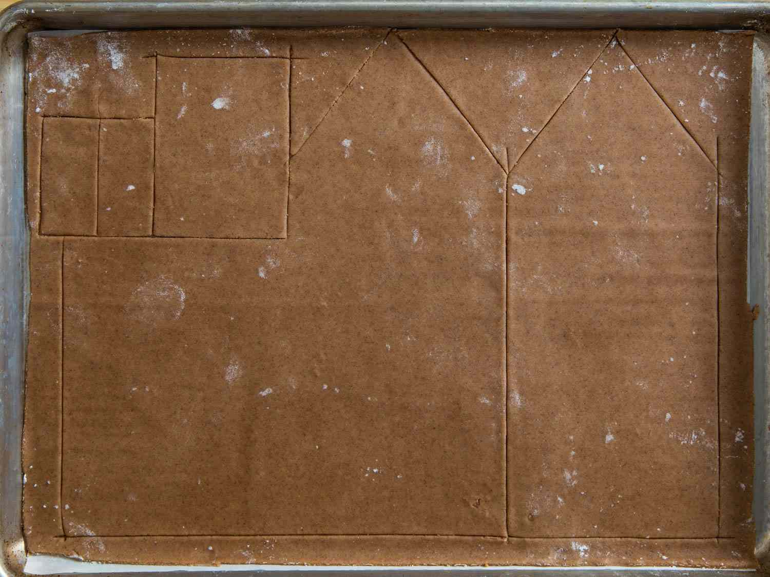 Construction ginger bread in a parchment-lined sheetpan, with some of the shapes cut into it.