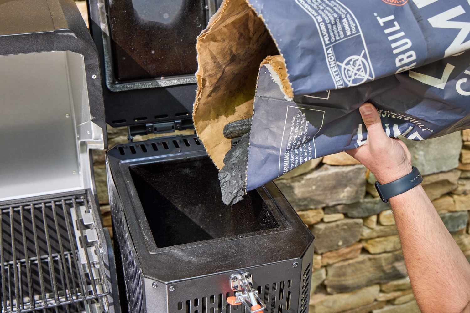 A person pours charcoal into the Masterbuilt Gravity Series 1150 Digital Charcoal Grill and Smoker