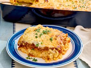 A serving of baked spaghetti on a plate garnished with herbs with a baking dish in the background