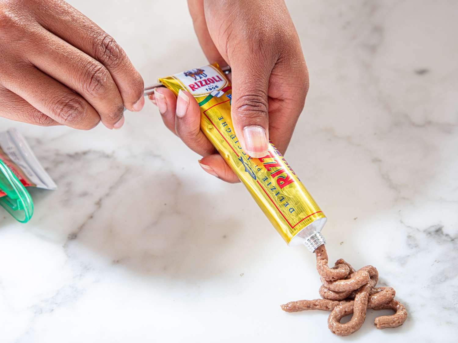 Hands squeezing brown paste out of a tube resembling toothpaste onto a surface
