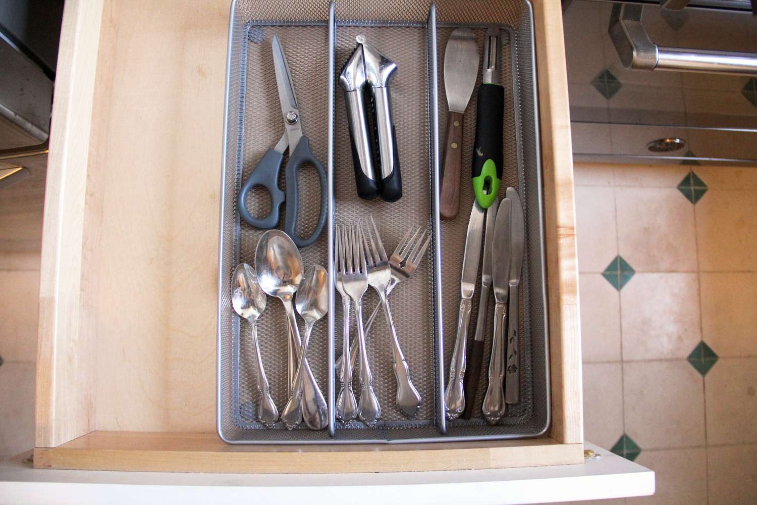 A mesh kitchen storage drawer with kitchen utensils and flatware in it.