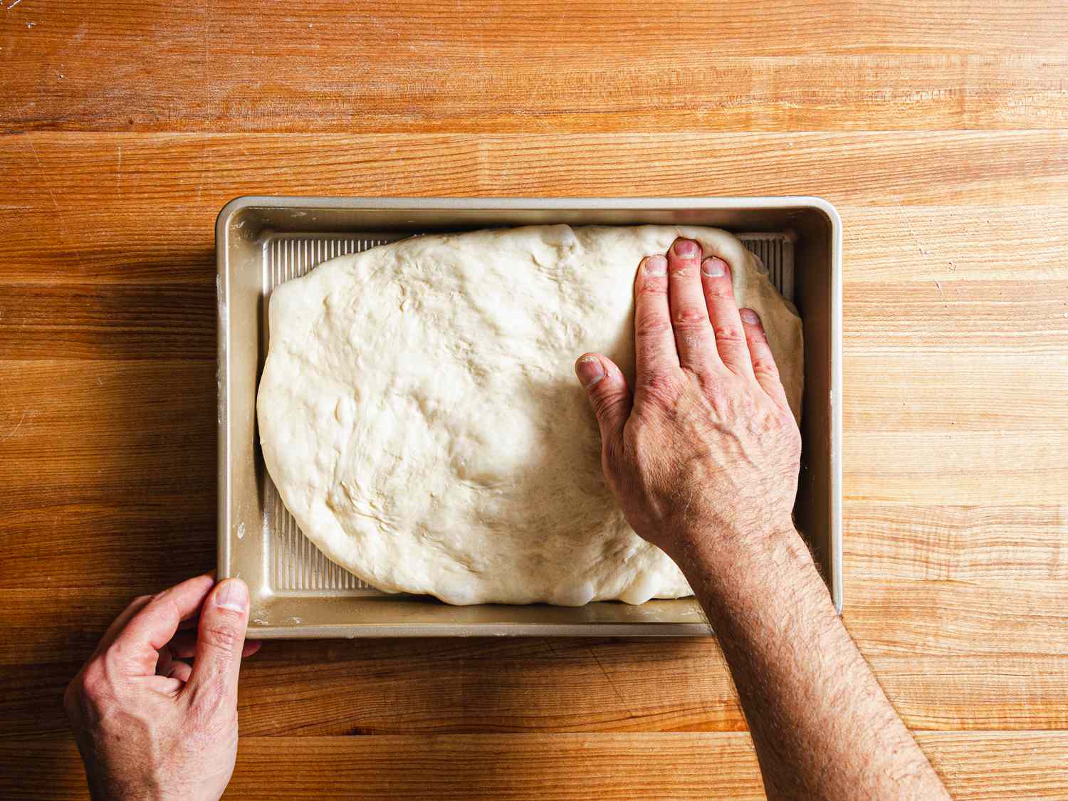 Two hands gently pushing dough to fill baking pan