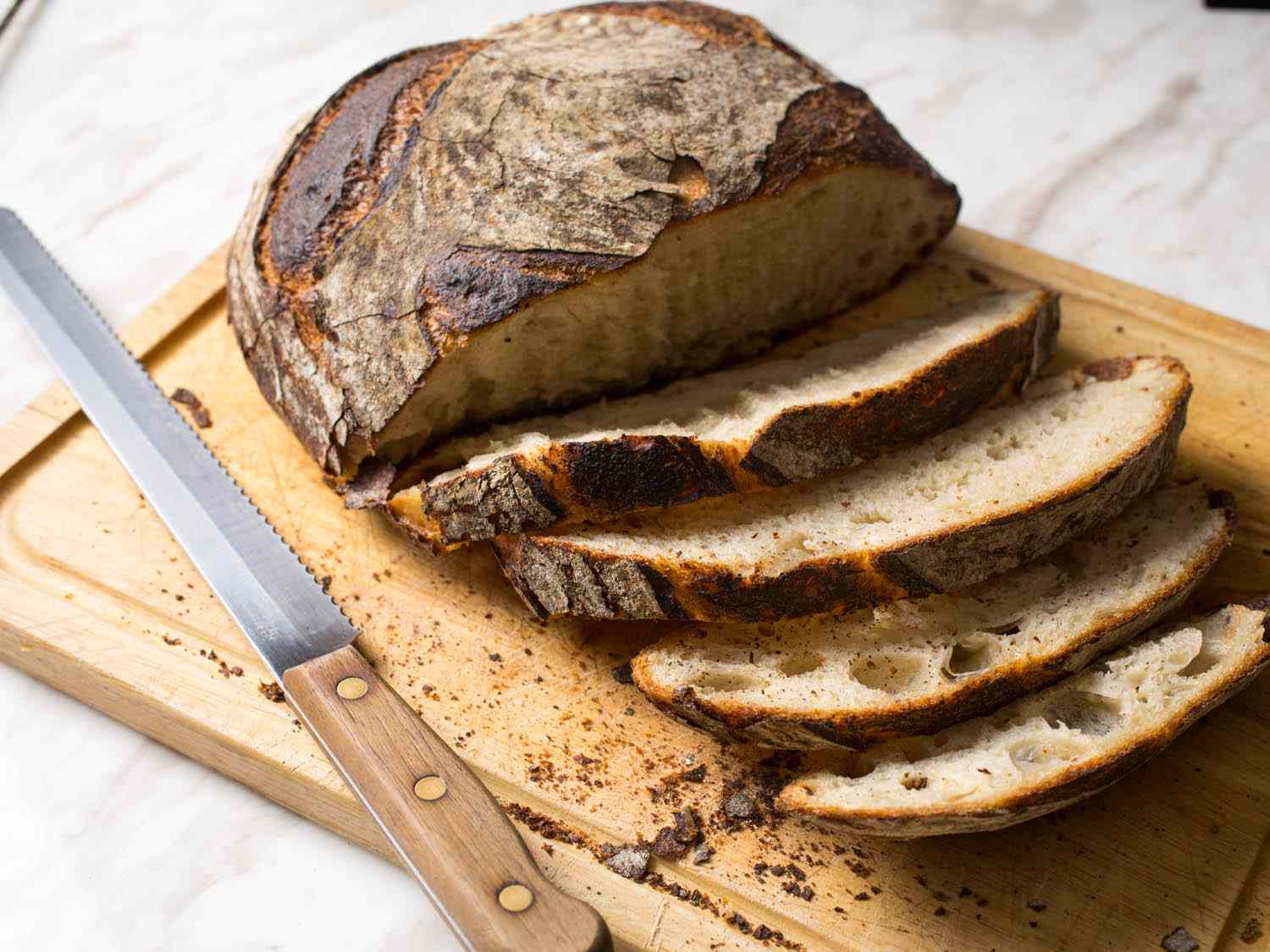 Bread loaf on cutting board with a bread knife beside it and several slices cut