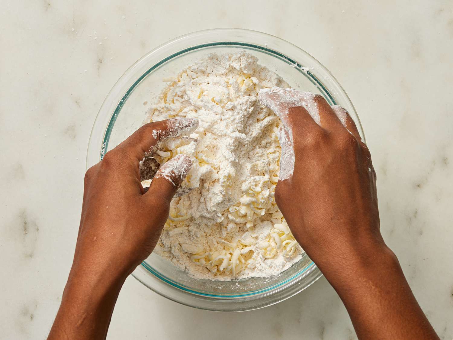 tossing butter and dry ingredients together with hands in a glass bowl 