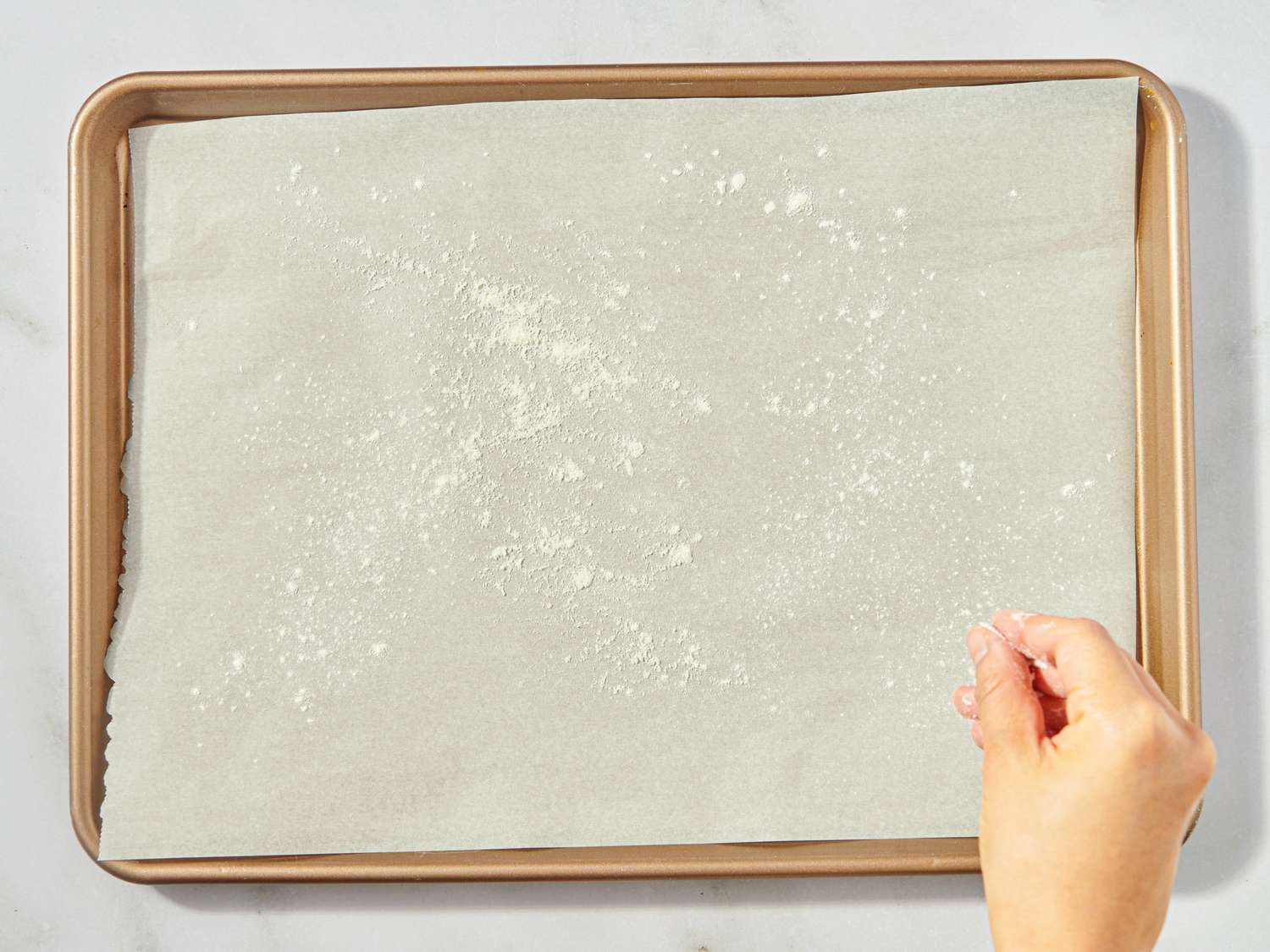 A hand sprinkling flour over a parchmentlined baking tray