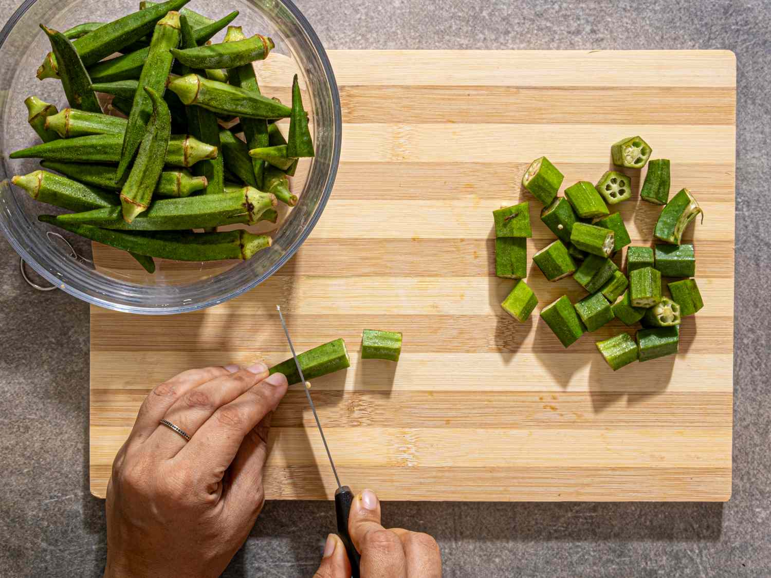 Preparing okra hands chopping okra on a cutting board with additional okra in a bowl