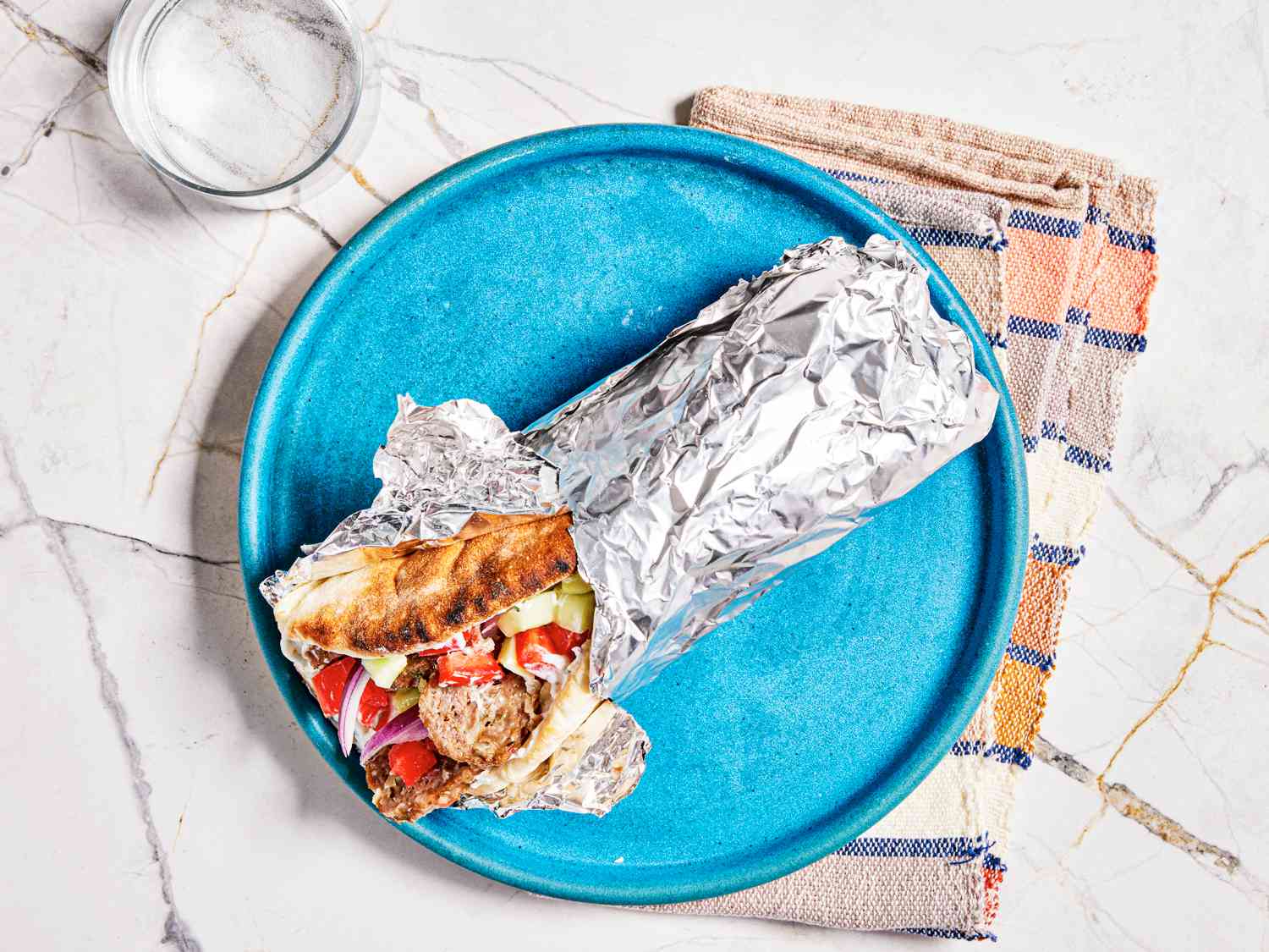 Finished gyro sandwich wrapped in aluminum foil on a bright blue plate 