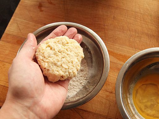 A hand holding a crab patty about to be coated with breadcrumbs. 