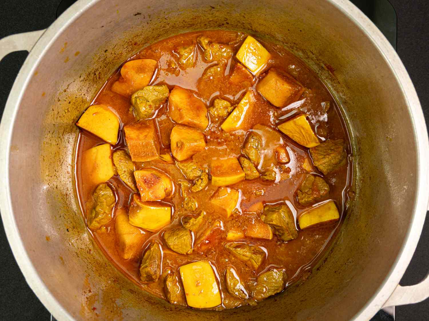 A pot of Persian stew with pieces of beef and sliced quince in a rich broth viewed from above