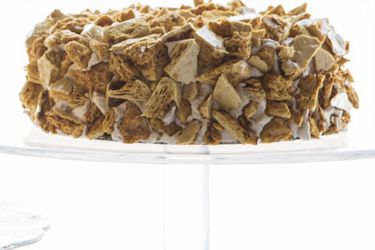 A loaf of Blum's Coffee Crunch Cake on a glass cake stand. The cake is covered with shards of honeycomb candy on all sides. 