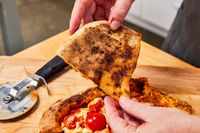 A hand holding a piece of pizza showing the underside 