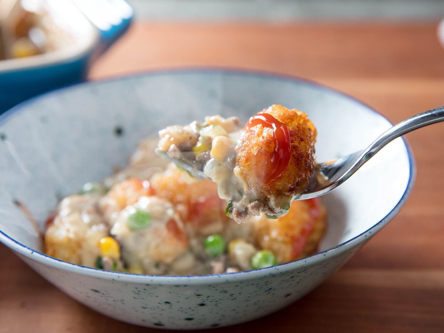 Fork digging into a bowl of tater tot hotdish.