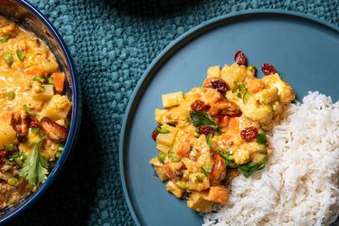 Overhead view of a portion of vegetable qorma served next to white rice on a blue plate, on a textured blue fabric