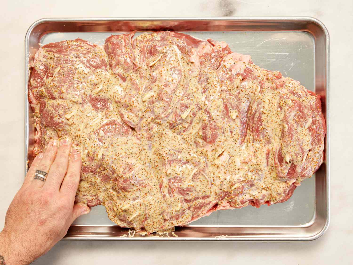 Overhead view of rubbing mustard sauce all over butterflied lamb