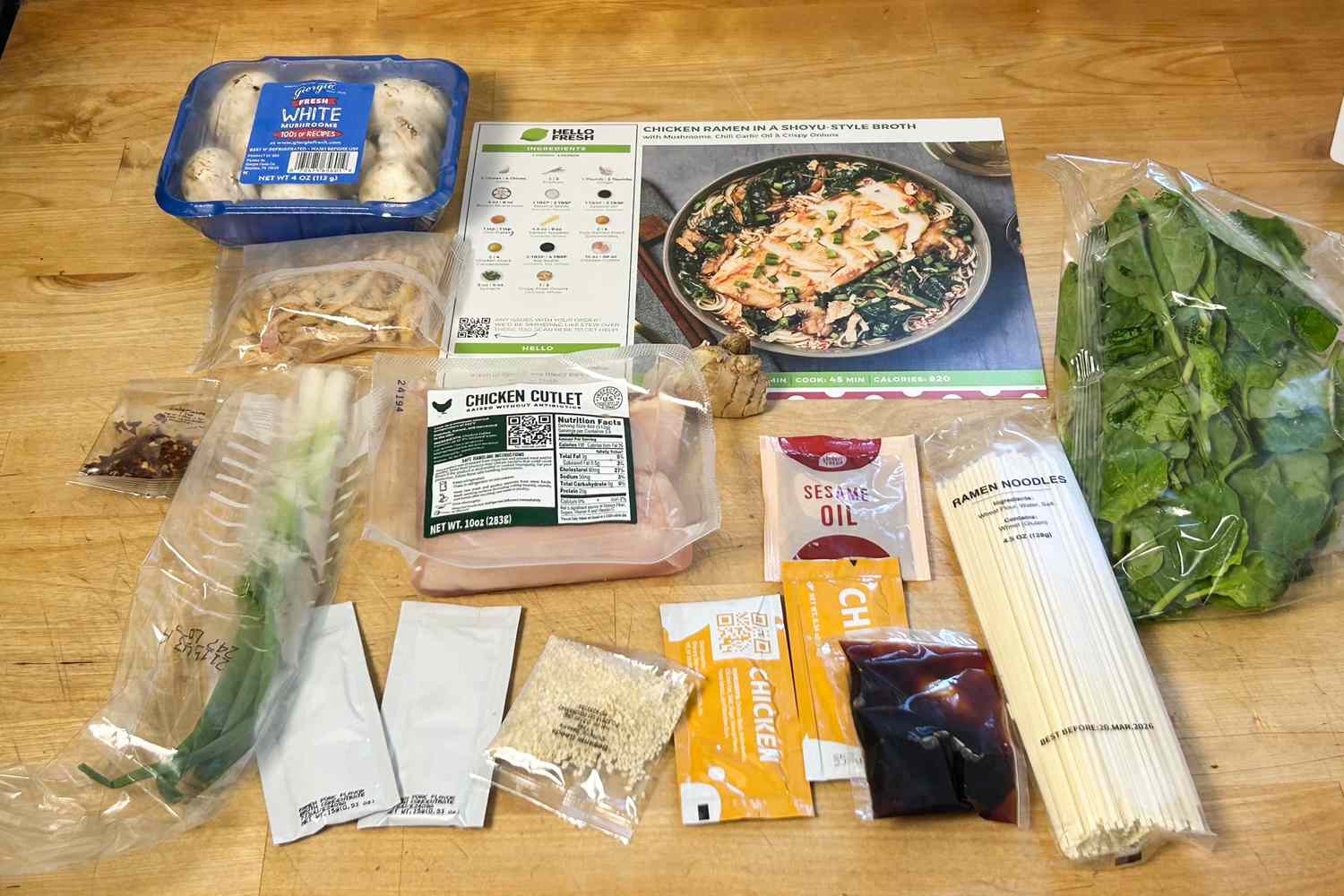 Meal kit ingredients for a ramen dish with recipe card on a wooden surface