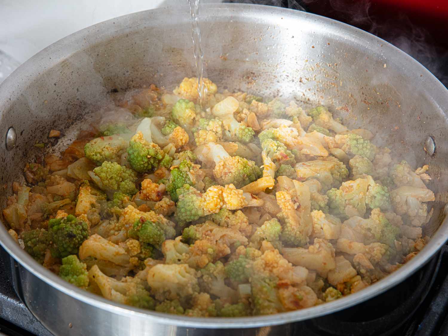 A pan of romanesco broccoli cooking on a stovetop with steam rising part of a pasta dish preparation