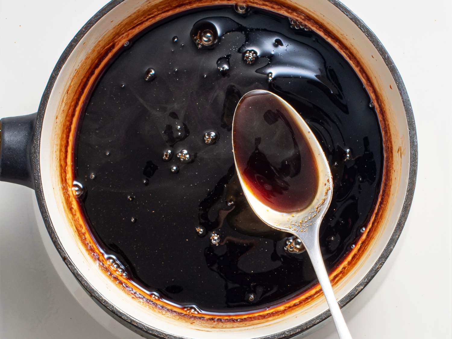 Thickened sweet tamarind chutney being lifted out of the cooking pot with a metal spoon to show its consistency.