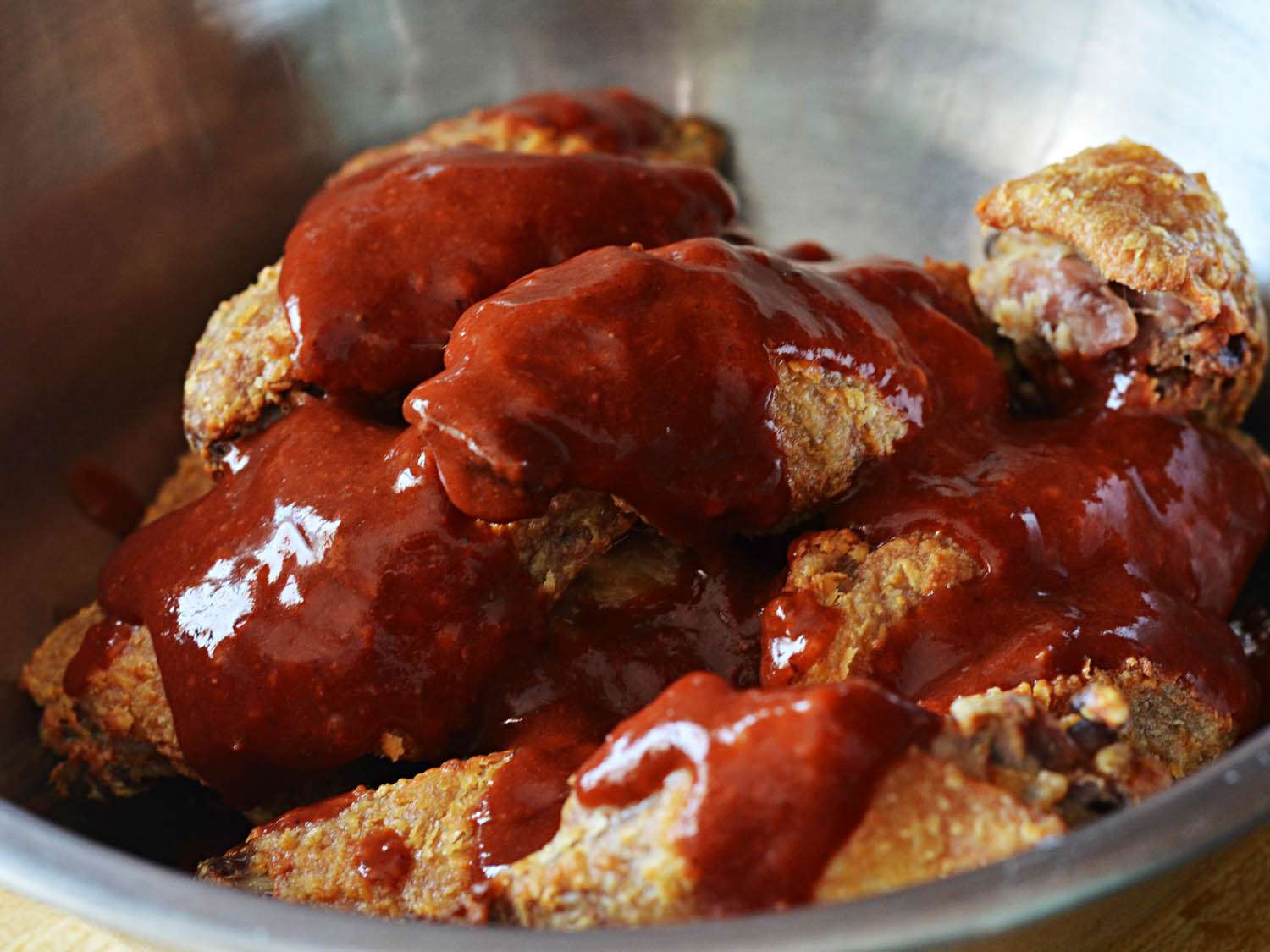 Oven-fried chicken wings covered in red sauce in silver bowl.