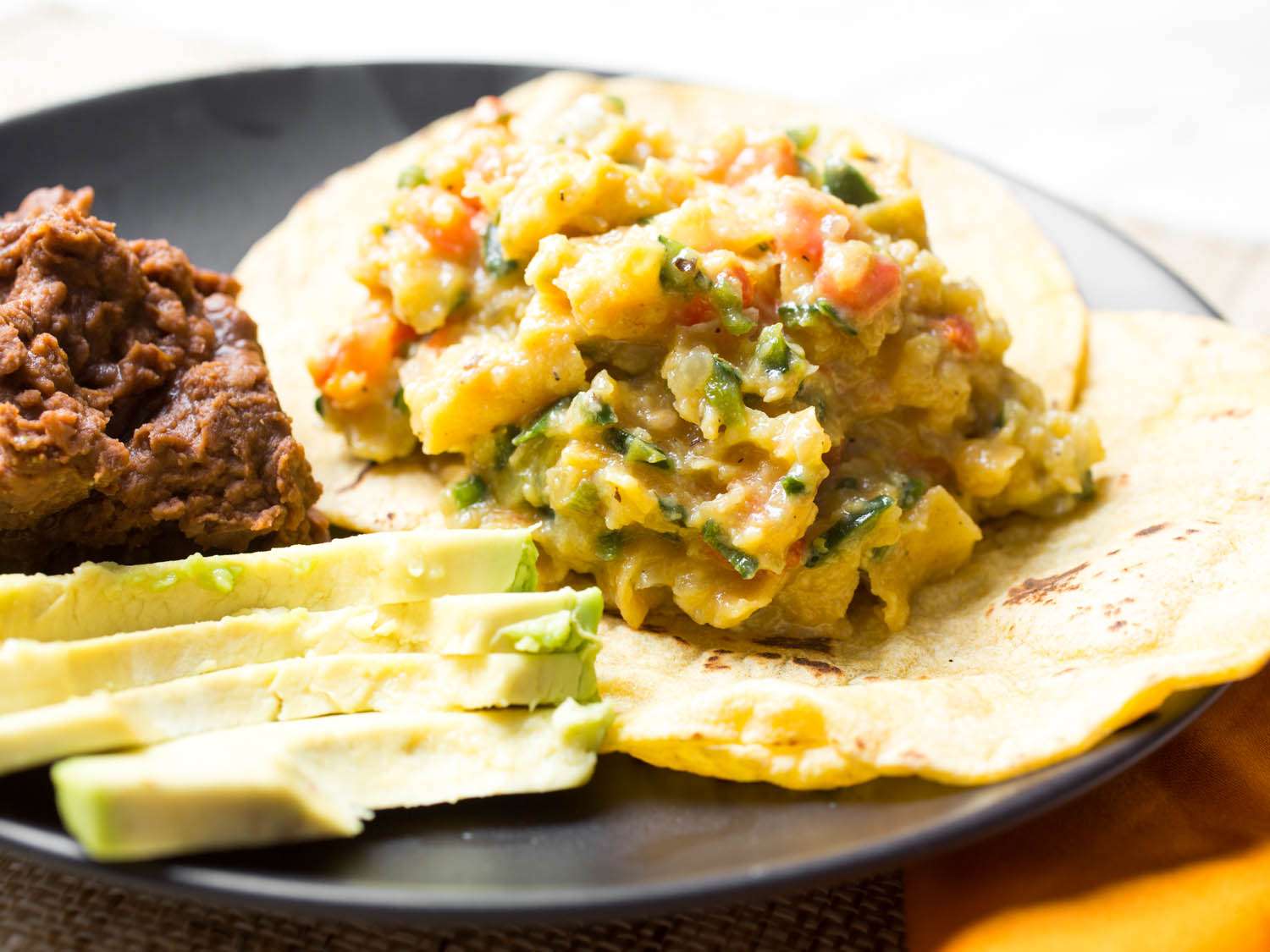 Finished Tex-Mex migas on a tortilla next to refried beans and sliced avocado.