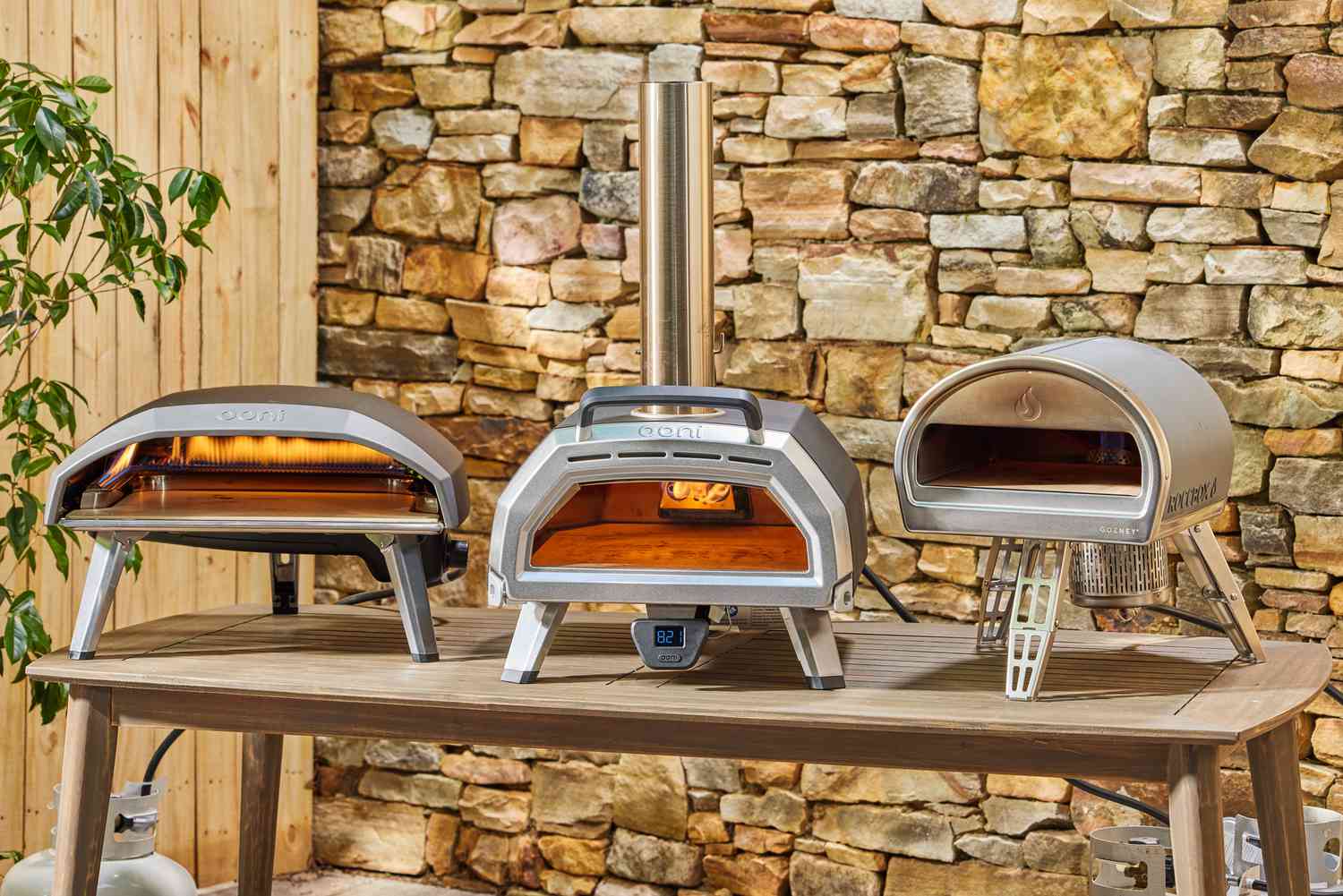 Three outdoor pizza ovens on a wooden table.