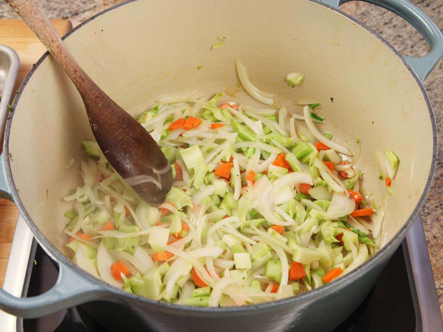 Sauteeing onions, carrots, and broccoli stems in a Dutch oven.