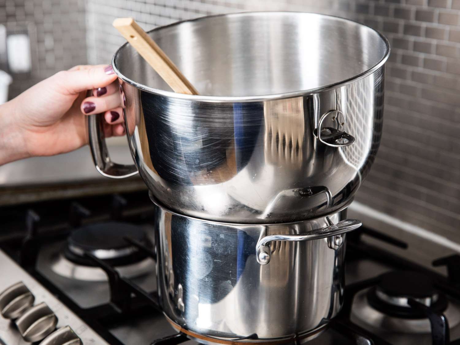 The author holds a stand mixer bowl over a pot of simmering water.