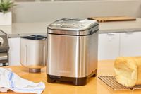 The Cuisinart CBK-110 Compact Automatic Bread Maker on a wooden counter next to baked bread