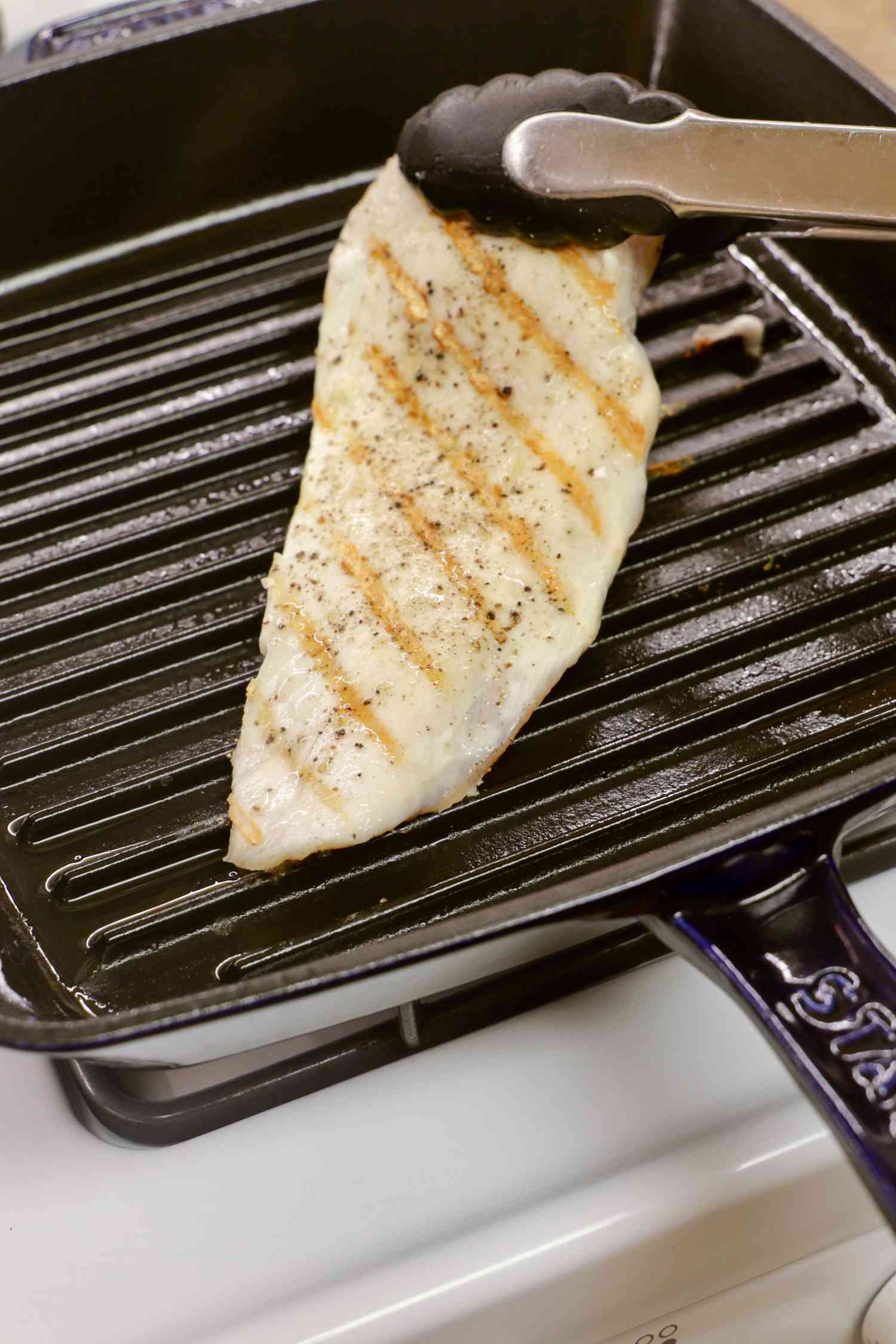 A person flipping a pork chop using tongs on the Staub Enameled Cast Iron Grill Pan