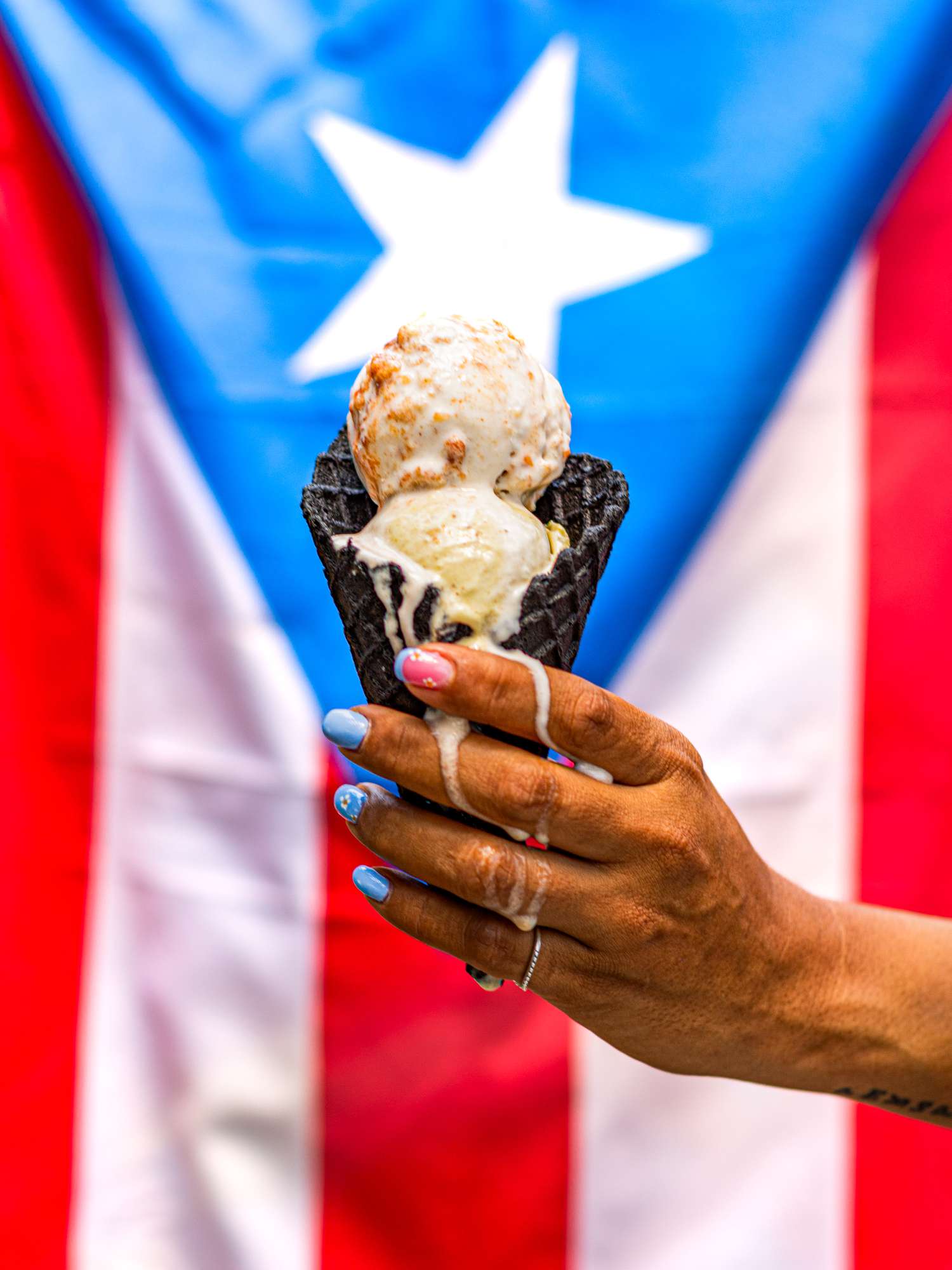 A soursop ice cream in charcoal cone from Via Lactea in front of a Puerto Rican flag
