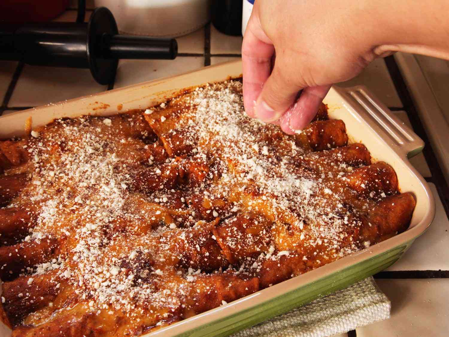 Sprinkling cotija cheese on top of chicken enchilada. 