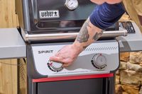 A hand turning a nob on the Weber Spirit E-210 Gas Grill
