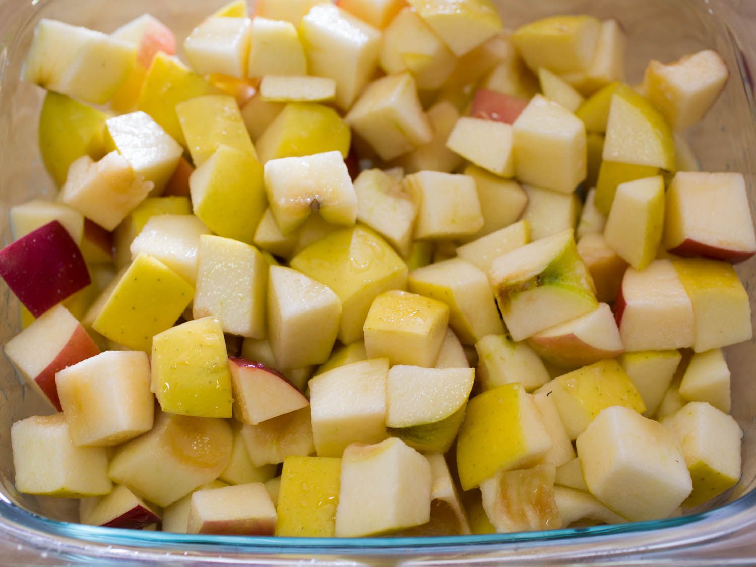 Chopped red and yellow apples in a glass baking dish.
