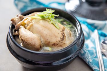 A bowl of samgyetang, with the whole poached Cornish hen, broth, and fresh scallion topping