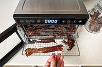 A person pulling racks of beef jerky from the Cosori food dehydrator