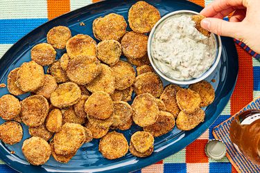 Blue platter with fried pickle and a small bowl of dip, with a hand dipping one pickle 