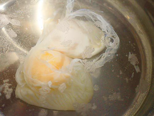 Two eggs poaching in water.