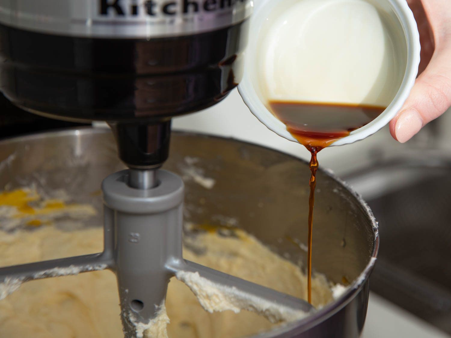 Pouring vanilla extract into cake batter being mixed in a Kitchenaid.