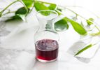 A small glass carafe partially filled with cherry pit syrup. There's a plant vine behind the carafe.