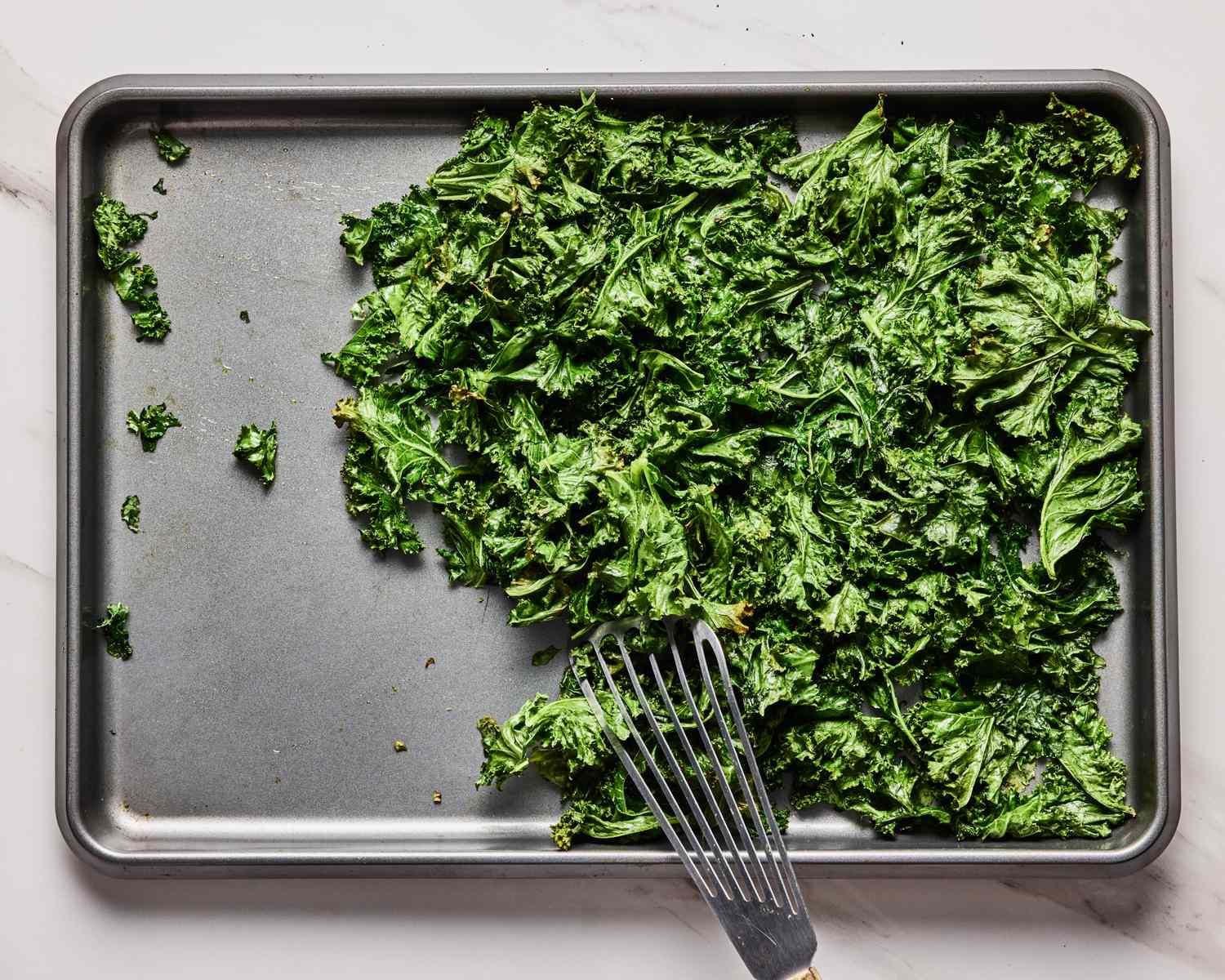 A baking tray with roasted greens and a spatula