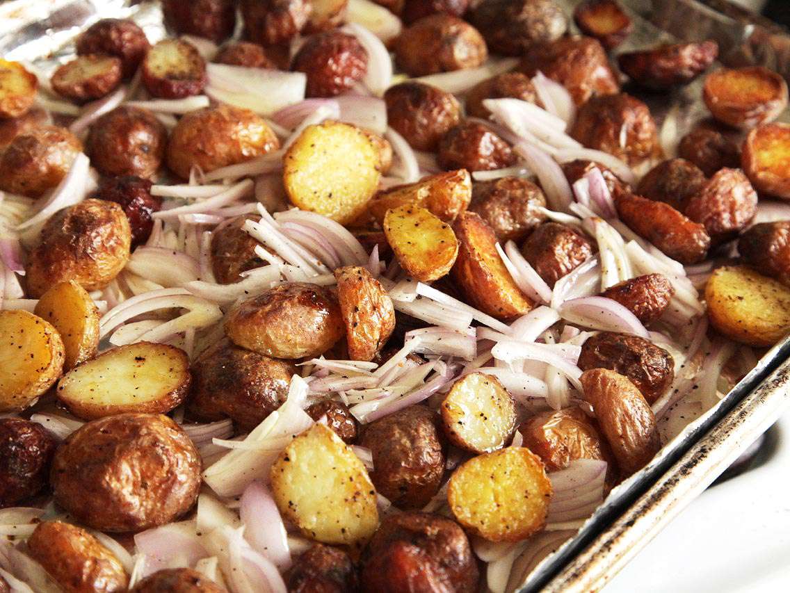 Roasted new potatoes on baking sheet with sliced raw shallots.