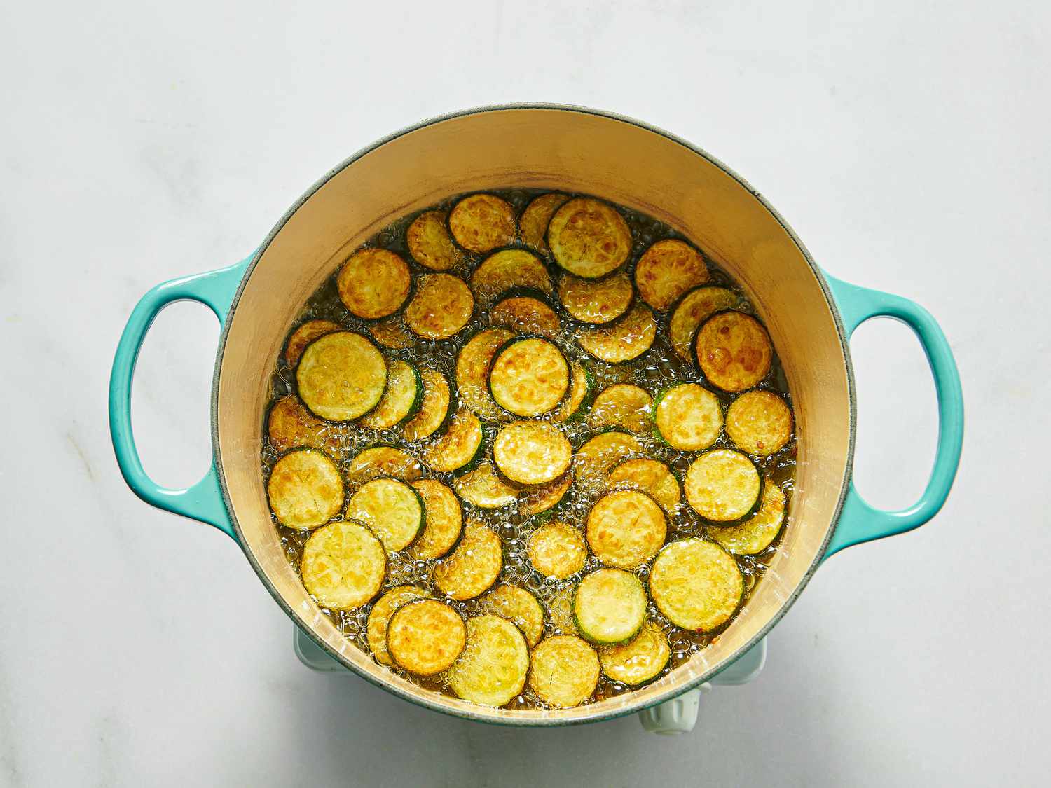 Slices of zucchini frying in a large pot with light oil, preparation for a recipe