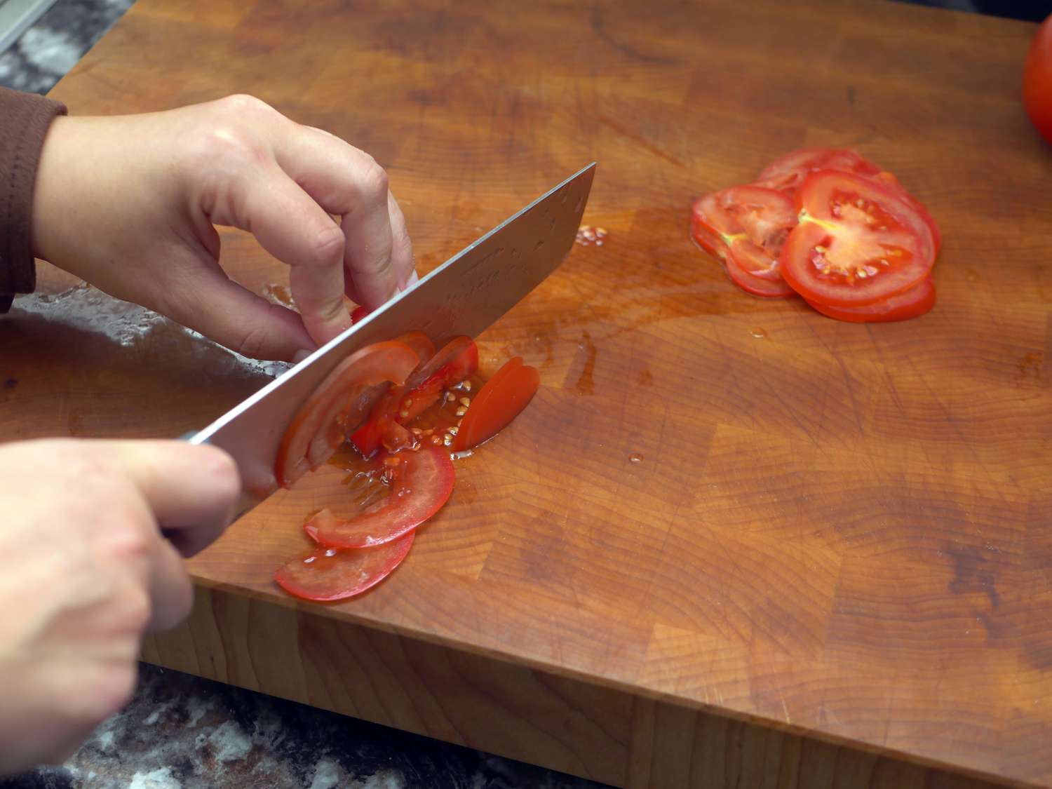 someone cutting a tomato on a wooden cutting board 